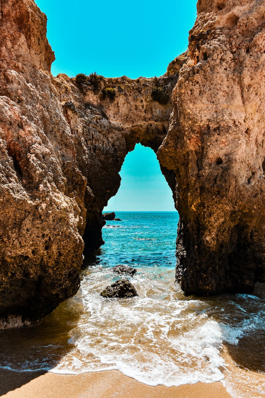 photo of rock formation near seashore under blue sky