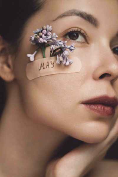 close up portrait of a woman with flowers tucked behind a band aid stuck to her cheek